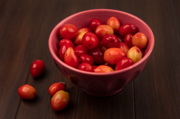 Top view of pale red sour cornelian cherries on a bowl on a wooden surface