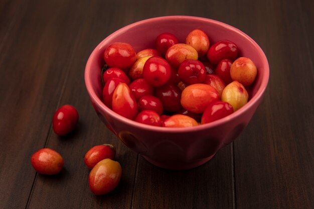 Top view of pale red sour cornelian cherries on a bowl on a wooden surface