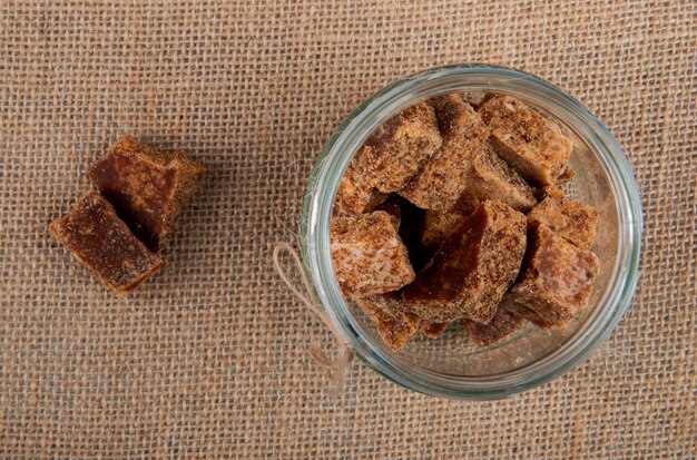Top view of palm sugar cubes in a glass jar on sackcloth texture background