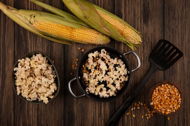 Top view of pan with delicious popcorns with corn kernels with fresh corns isolated on a wooden bowl on a wooden table