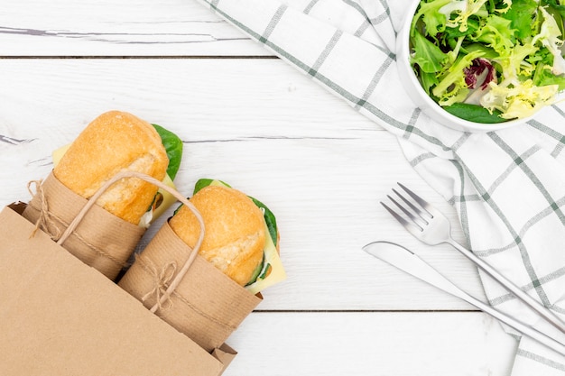 Вид сверху бумажный пакет с двумя бутербродами внутри и салат