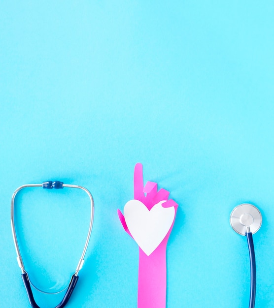 Free photo top view of paper hand holding heart with stethoscope and copy space