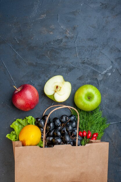 Top view paper shopping bag apples black grapes lemon greens on dark table free space