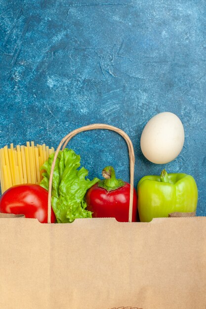 Top view paper shopping bag egg tomato spaghetti lettuce bell peppers on blue table free space