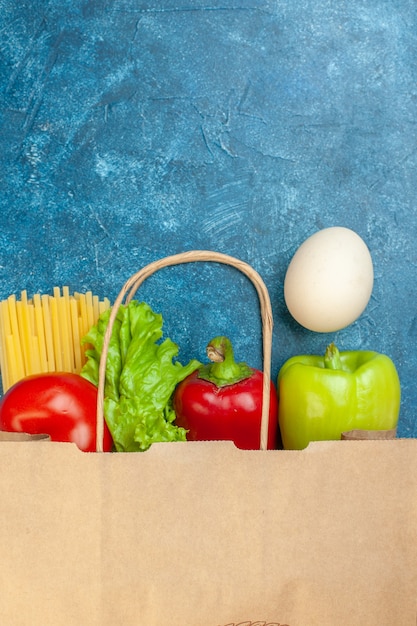 Бесплатное фото Вид сверху бумажная сумка для покупок яйцо, помидоры, спагетти, салат, болгарский перец на синем столе, свободное пространство