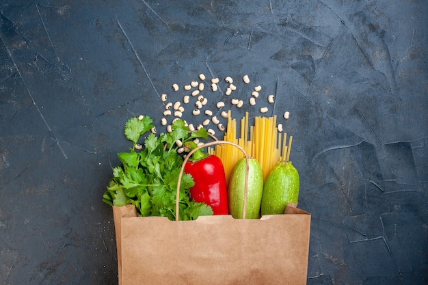 Top view paper shopping bag spaghetti red bell pepper zucchini coriander beans on dark table free space