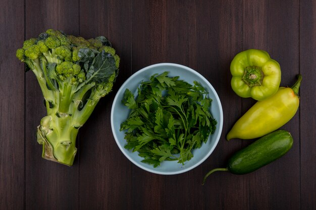 Top view parsley in bowl with broccoli  cucumber and peppers on wooden background