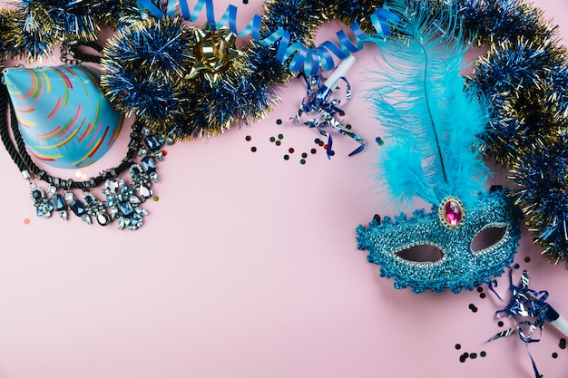 Top view of party hat; tinsel; necklace with confetti and blue masquerade carnival feather mask
