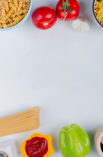 Top view of pasta in bowls, garlic and tomatoes