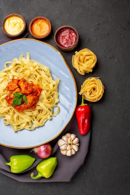 Top view pasta bowls of sauces pasta colorful ball pepper garlic onion next to the plate of pasta with meat on the tablecloth