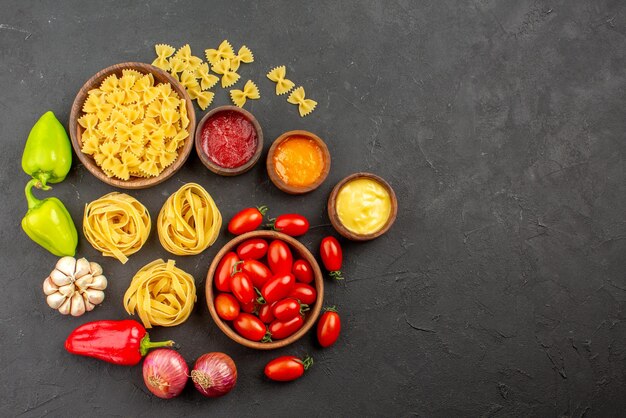 Top view pasta and pepper bowls of pasta and tomatoes red and green bell pepper onion garlic three kind of sauces on the table