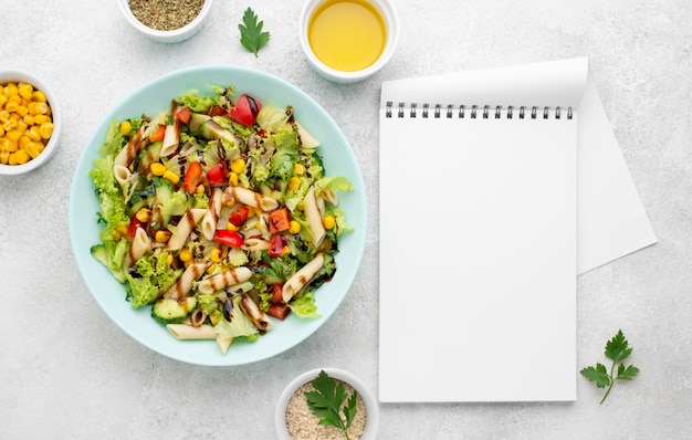 Top view pasta salad with balsamic vinegar and blank notebook