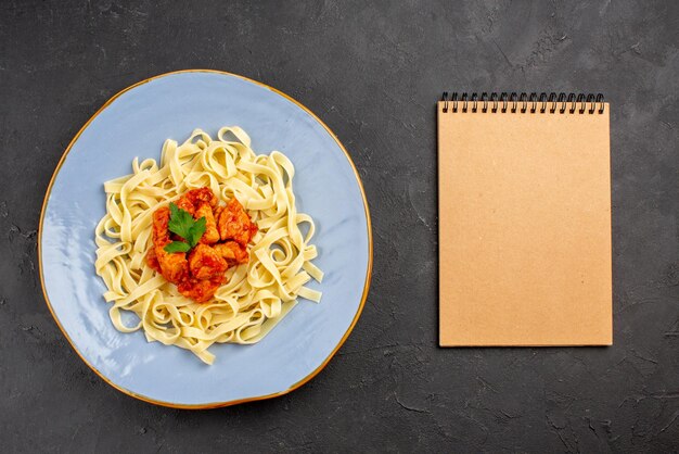 テーブルの上のクリームノートの横にある肉汁と肉の食欲をそそるパスタのミートブループレートの上面パスタ