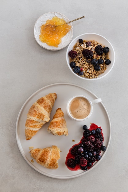 Vista dall'alto prodotti di pasticceria nel vassoio con una tazza di caffè, olive, lamponi, marmellata di frutta, noci sulla superficie bianca. verticale