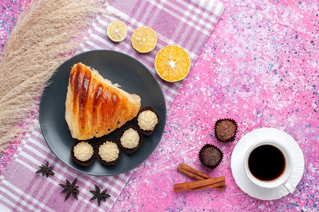 Top view of pastry slice with cinnamon, cup of tea and chocolate candies on pink surface