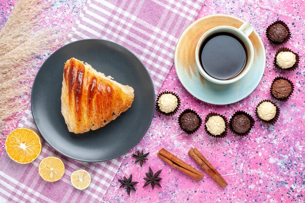 Top view of pastry slice with cup of tea and chocolate candies on the light pink surface