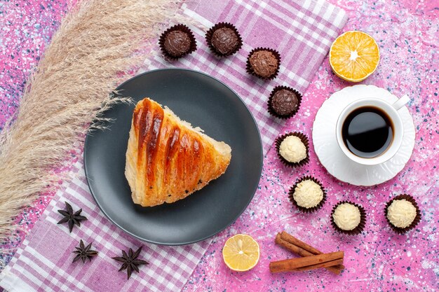 Top view of pastry slice with cup of tea and chocolate candies on pink surface