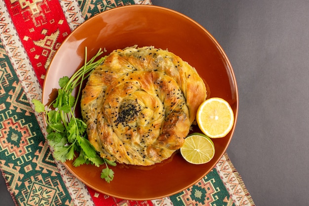 Top view of pastry with meat delicious dough meal inside brown plate with lemon slices on the dark surface