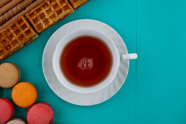 Top view of pattern of cookies and crispy sticks cakes with cup of tea on blue background with copy space