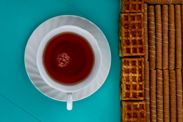 Top view of pattern of crispy sticks and cakes with cup of tea on blue background