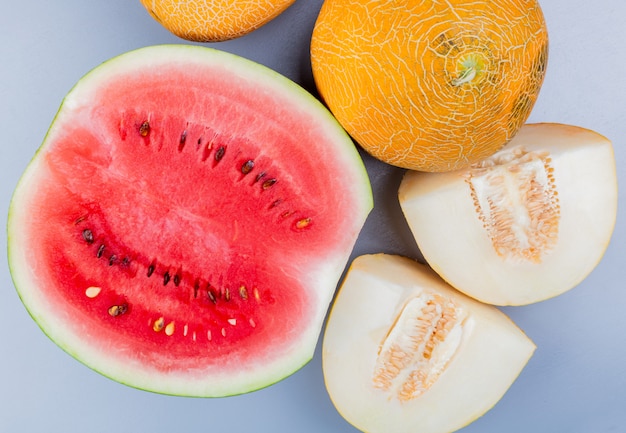 Top view of pattern of cut and whole fruits as watermelon and melon on bluish gray background