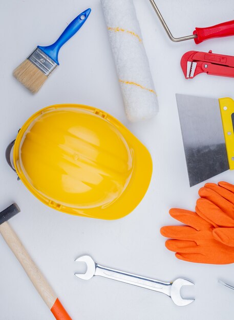 Top view of pattern from set of construction tools as brick hammer pipe wrench safety helmet putty knife paintroller paintbrush and open-end wrench on white background