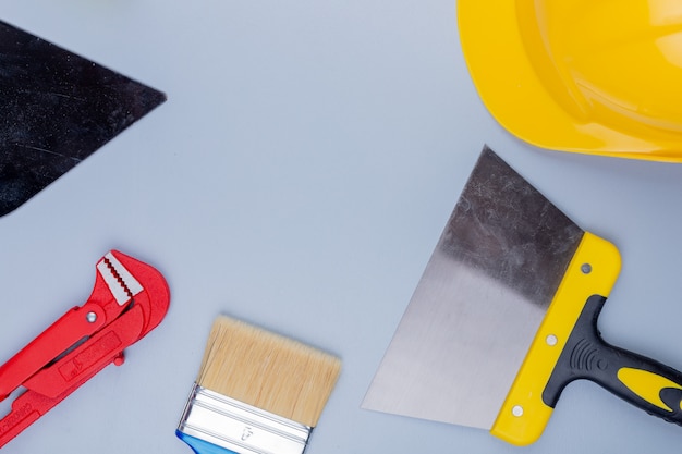 Foto gratuita vista superiore del modello dall'insieme degli strumenti della costruzione come pennello della spatola del casco di sicurezza della chiave stringitubo e coltello di mastice su fondo grigio