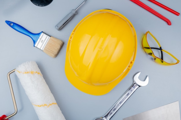 Vista dall'alto del modello dal set di strumenti di costruzione come cacciavite occhiali di sicurezza casco di sicurezza coltello stucco rullo di vernice pennello e chiave a forchetta su sfondo grigio