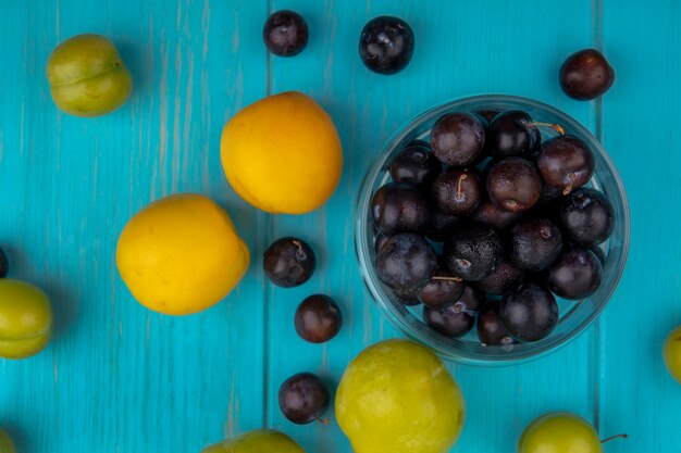 Вид сверху на узор из фруктов в виде нектакотов, зеленых слив и виноградных ягод с чашей виноградных ягод на синем фоне