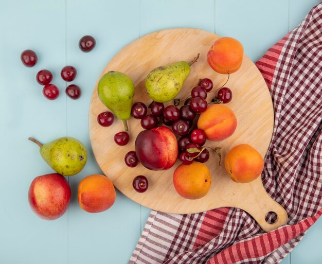 Top view of pattern of fruits as peach pear apricot cherry on cutting board on plaid cloth and on blue background