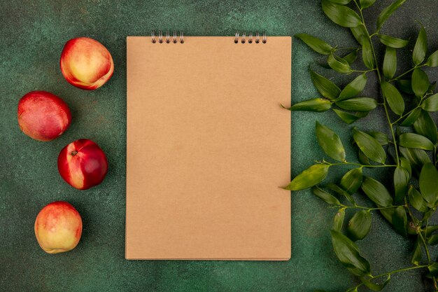 Top view of pattern of peaches with note pad and leaves on green background with copy space