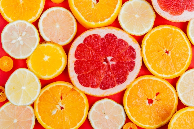 Top view of pattern of sliced citrus fruits as orange grapefruit lemon on red table