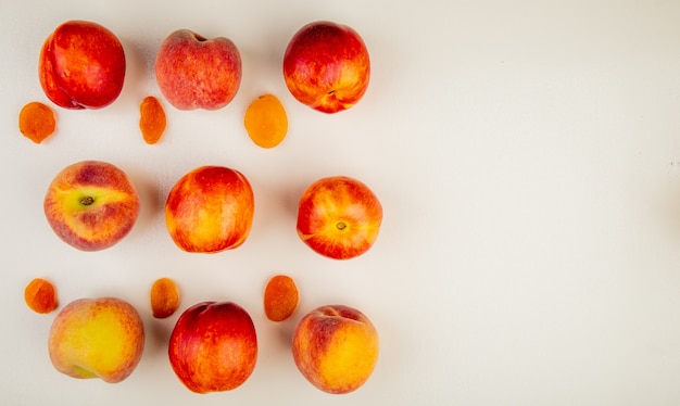 Top view of pattern of sliced and whole peaches on left side and white surface with copy space