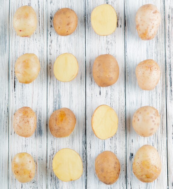 Top view of pattern of whole and cut potatoes on wooden background