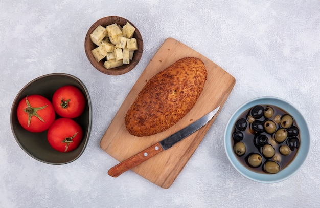 Top view of patty on a wooden kitchen board with knife with cheese tomatoes and olives on a white background