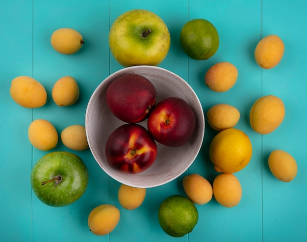 Top view of peaches in a bowl with apples apricots lemon and lime on a blue surface