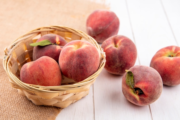 Top view of peaches on a bucket on sack cloth with peaches isolated on white surface
