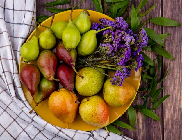 Top view of peaches and flowers in plate on plaid cloth and wooden surface decorated with leaves