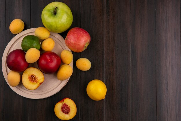 Top view of peaches on a stand with apricots and apples on a wooden surface