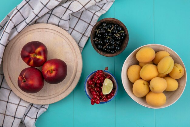 Top view of peaches on a stand with red and black currants and with apricots on a blue surface