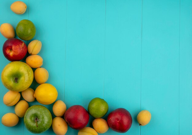 Вид сверху персиков с яблоками, абрикосами, лимоном и лаймом на синей поверхности