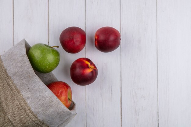白い表面に黄麻布の袋にリンゴと桃のトップビュー