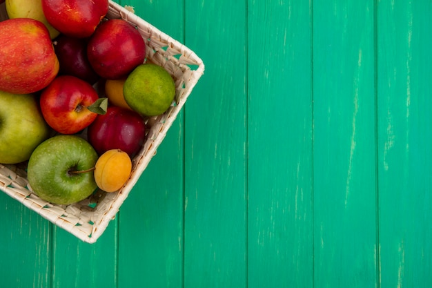 Free photo top view of peaches with apples and lime in a basket on a green surface