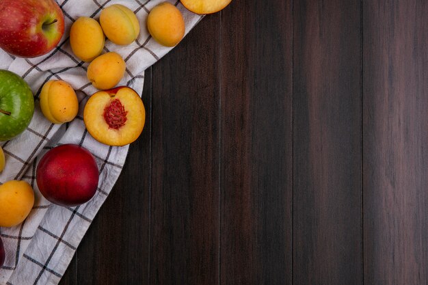 Top view of peaches with apricots and apples on a towel on a wooden surface