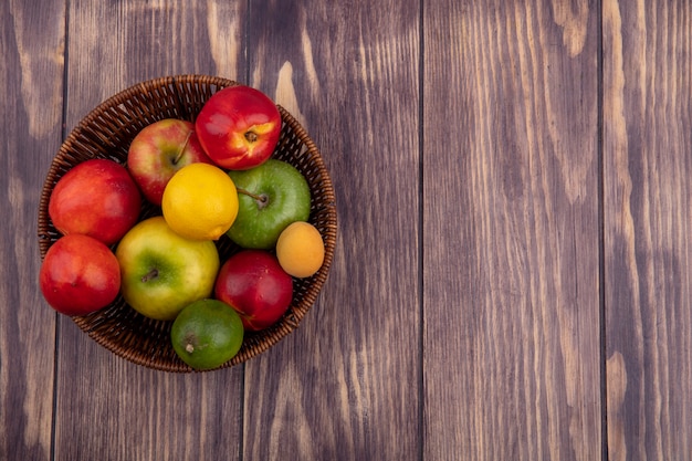 Top view of peaches with colored apples in a basket on a wooden surface