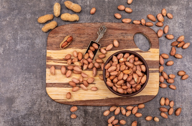 Top view peanuts in bowl on wooden cutting board on stone  horizontal