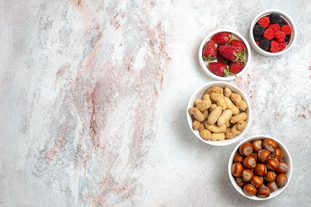 Free photo top view of peanuts and hazelnuts with fresh strawberries on the white surface