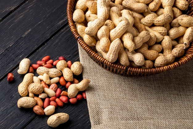 top view peanuts in shell in a basket with peeled on a black wooden table