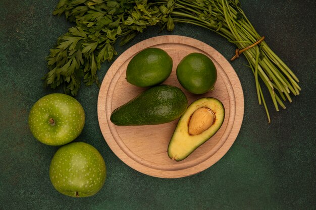 Top view of pear shaped avocados on a wooden kitchen board with limes with green apples and parsley isolated on a green background