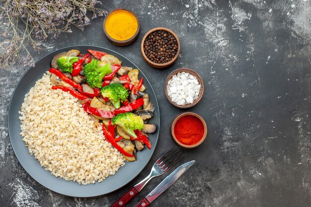 Top view pearl barley with tasty cooked vegetables and seasonings on grey table